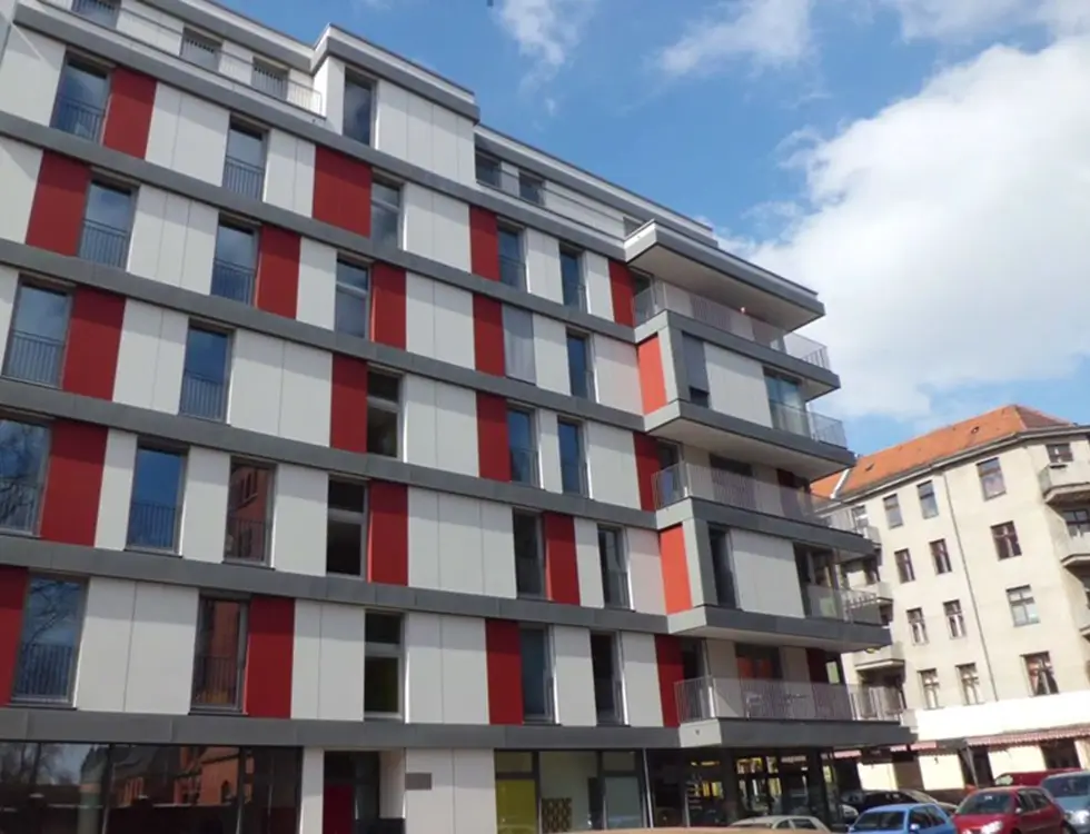 Ein mehrstöckiges Wohnhaus ist mit weißen, roten und orangen Fassadenelementen verkleidet